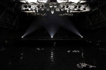 DARKNESS Produktionsfoto: Dunkle Bühne, drei Lichtspots, auf der Bühne liegen silberne Gegenstände, nicht näher erkennbar