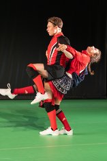 "Wir im Finale", ein Fußballspieler wird von einer Fußballspielerin hochgehoben und sitzt im Stand auf deren Schoß