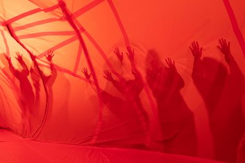 QUERBALKEN: Schatten von Personen auf oragefarbenen Tunnelwand aus dünnem Stoff